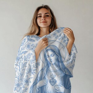 May include: A white throw blanket with a blue floral pattern and a blue image of the Virgin Mary holding a heart. The blanket is made of soft, comfortable fabric.