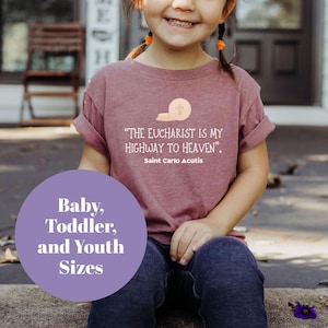 May include: A young child wearing a maroon t-shirt with the quote "THE EUCHARIST IS MY HIGHWAY TO HEAVEN." by Saint Carlo Acutis. The shirt is available in baby, toddler, and youth sizes.