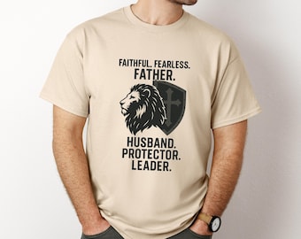 Op de afbeelding: Beige t-shirt met zwarte tekst en afbeelding. De tekst luidt: "FAITHFUL. FEARLESS. FATHER. HUSBAND. PROTECTOR. LEADER." Een leeuwenkop- en schildafbeelding staat onder het woord "FATHER".