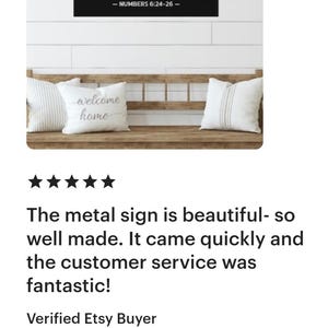 Op de afbeelding: Een zwart metalen bord met witte tekst met de tekst: "DE HERE zegene u en behoede u; DE HERE doe zijn aangezicht over u lichten en zij u genadig." - NUMBERS 6:24-26. Het bord staat boven een houten bank met kussens.