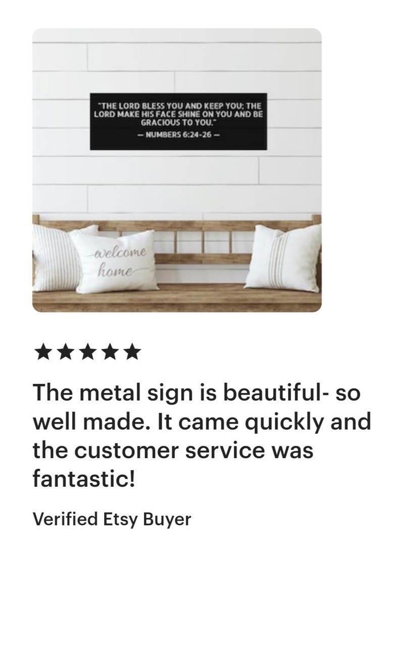 Op de afbeelding: Een zwart metalen bord met witte tekst met de tekst: "DE HERE zegene u en behoede u; DE HERE doe zijn aangezicht over u lichten en zij u genadig." - NUMBERS 6:24-26. Het bord staat boven een houten bank met kussens.