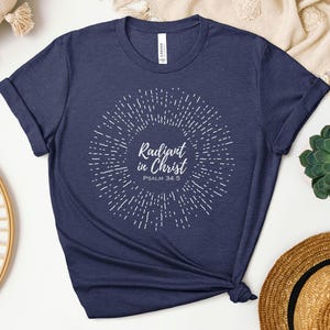 May include: Navy blue t-shirt with a white sunburst design and the text "Radiant in Christ Psalm 34:5".