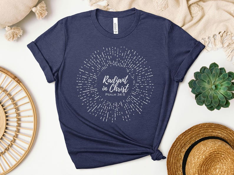 May include: Navy blue t-shirt with a white sunburst design and the text "Radiant in Christ Psalm 34:5".