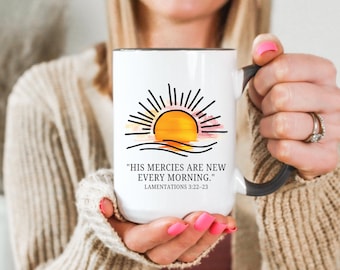 May include: White ceramic mug with a black rim and handle, featuring a sunrise design in yellow, orange, and pink, with the text "HIS MERCIES ARE NEW EVERY MORNING." Lamentations 3:22-23.