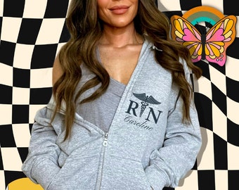 May include: A gray zippered hoodie with a black and white graphic of a caduceus and the text "RN Caroline".