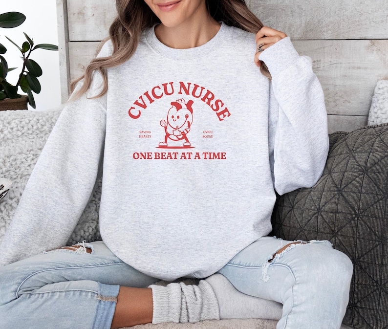 May include: A gray sweatshirt with the text "CVICU NURSE" in red, featuring a cartoon heart holding a stethoscope. The text "Saving Hearts, One Beat at a Time" is also in red.