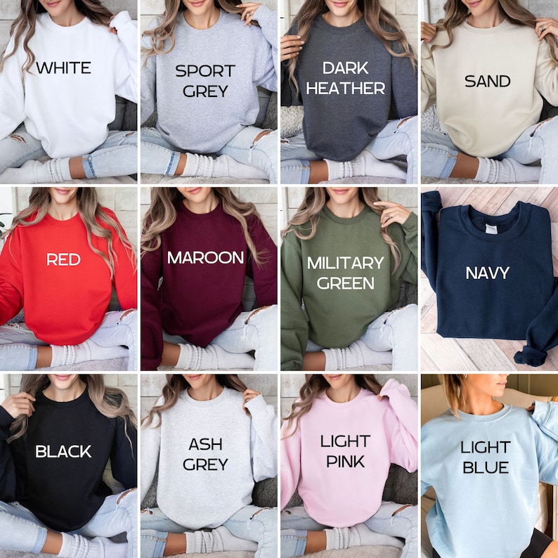 May include: Twelve different color sweatshirts with text on the front. The colors are white, sport grey, dark heather, sand, red, maroon, military green, navy, black, ash grey, light pink, and light blue. The text on the sweatshirts includes "White", "Sport Grey", "Dark Heather", "Sand", "Red", "Maroon", "Military Green", "Navy", "Black", "Ash Grey", "Light Pink", and "Light Blue".
