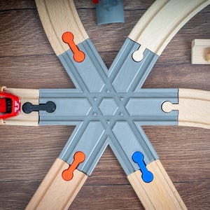 Op de afbeelding: Houten speelgoedtreinbaan met een rode speelgoedtrein, grijze kruising en kleurrijke connectoren. De baan is geplaatst op een houten oppervlak, met speelfiguren en accessoires.