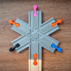 Könnte beinhalten: Ein graues, sternförmiges Holzspielzeug mit farbigen Stiften. Das Spielzeug hat orange, rosa, blaue und schwarze Stifte. Das Spielzeug liegt auf einer Holzoberfläche.