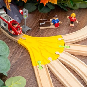 May include: A wooden toy train set with a red and white train, a yellow track switch, and miniature figures. The set includes a train station and a signal. The train is on a wooden track.