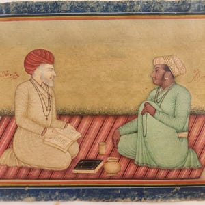 Könnte beinhalten: Antike indische Miniaturmalerei, die zwei Figuren in traditioneller Kleidung zeigt, die auf einem gestreiften Teppich sitzen. Eine Figur trägt einen roten Turban und hält ein Buch, die andere einen grünen Robe. Ein kleiner Topf und eine Tasse befinden sich auf dem Teppich.