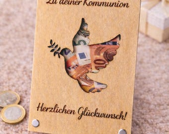 Puede incluir: Tarjeta de madera con un recorte de paloma relleno de billetes de euro. La tarjeta tiene el texto "Zu deiner Kommunion" y "Herzlichen Glückwunsch!" en escritura negra. Remaches plateados aseguran la tarjeta.