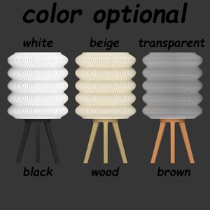K&ouml;nnte beinhalten: Drei moderne Lampen mit plissierten Schirmen in Wei&szlig;, Beige und Transparent. Jede Lampe hat ein Stativgestell in Schwarz, Holz und Braun. Der Text "color optional" steht oben.