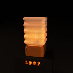 May include: An illuminated orange lamp with a textured, wavy shade and a square base. The lamp emits a warm glow. The number "1997" is displayed in orange on a black surface below the lamp. The measurements are in centimeters.