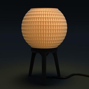 May include: A spherical table lamp with a textured, grid-like pattern on the shade. The lamp emits a warm, inviting glow. It sits on a black, tripod-style base. The lamp's cord extends to the right.