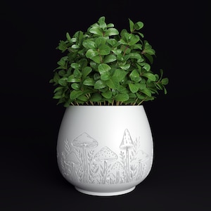May include: A white ceramic plant pot with a detailed relief design of mushrooms and foliage. The pot is filled with vibrant green leafy plants. The pot is approximately 8 inches tall and 7 inches wide, set against a black background.