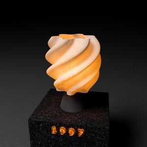 May include: A modern, abstract lamp with a swirling, textured design. The lamp emits a warm, orange glow and is mounted on a black, textured base. The year "1997" is illuminated on the base.