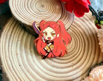 May include: A rose gold enamel pin featuring a cartoon character with red hair in pigtails, holding a purple and silver weapon. The character is wearing a black outfit with a yellow and gold skirt. The pin is on a wooden surface.