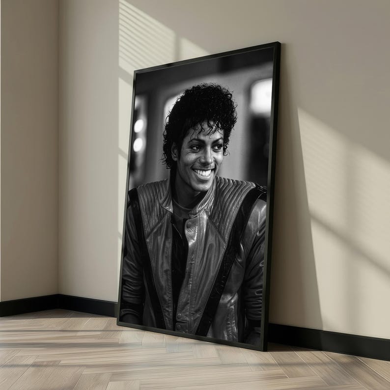May include: Black and white framed portrait of a smiling man with curly hair. He is wearing a leather jacket with a high collar. The portrait is leaning against a wall.