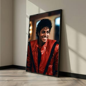 May include: Framed portrait of a smiling person with dark curly hair, wearing a red leather jacket with black accents. The portrait is displayed in a black frame, leaning against a wall.