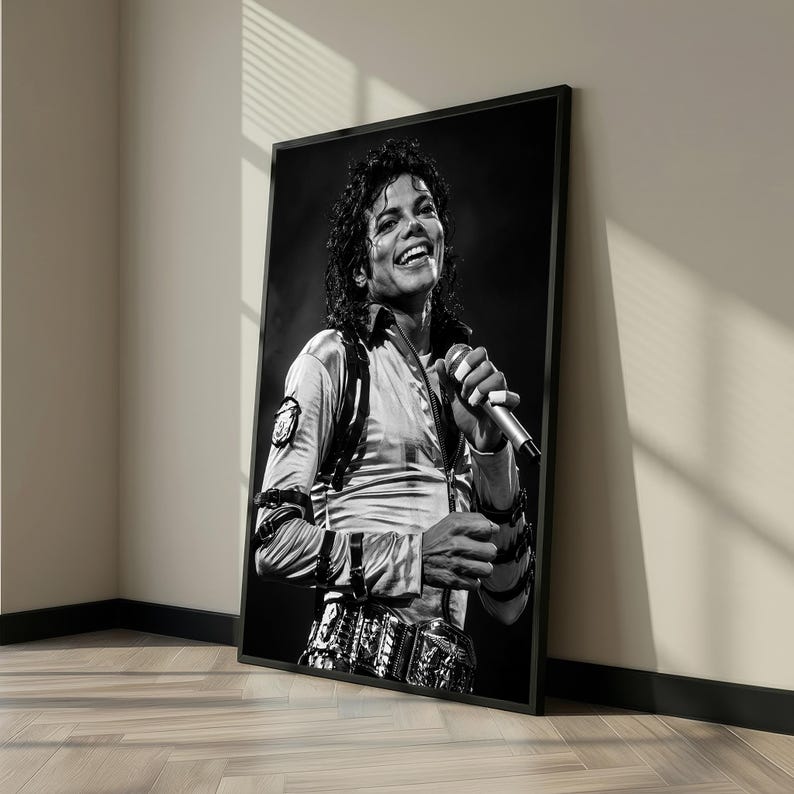 May include: Black and white framed print of a smiling person holding a microphone. The person is wearing a light-colored shirt with a detailed belt and wrist cuffs. The image is leaning against a wall.