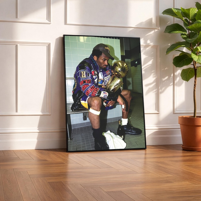 May include: Framed print featuring a seated figure holding a golden trophy. The figure wears a purple and yellow jacket with patches and a baseball cap. The image is set against a tiled wall.