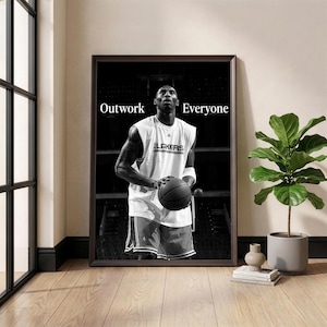 May include: Framed monochrome print of a basketball player holding a ball. The player wears a white vest with "Lakers" on it. The words "Outwork Everyone" are printed above the player's head in white text.