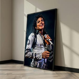 May include: Framed portrait of Michael Jackson in a silver and black outfit, holding a microphone and smiling. The image is set against a dark background, with the frame leaning against a wall and floor.