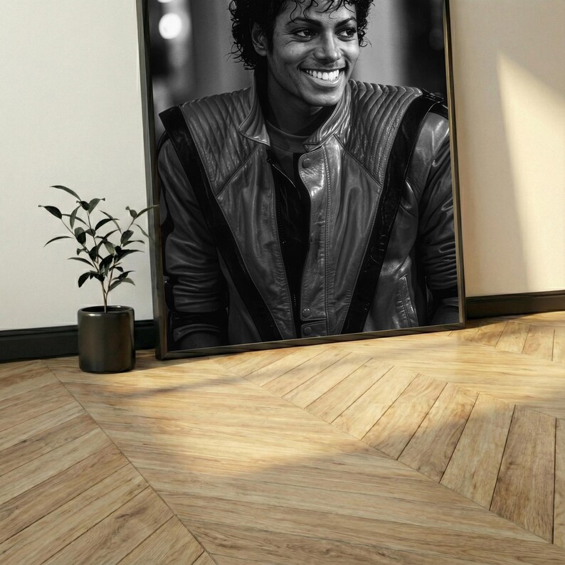May include: Black and white framed portrait of Michael Jackson smiling. He is wearing a black leather jacket with black stripes. A small potted plant sits to the left of the portrait on a wooden floor.