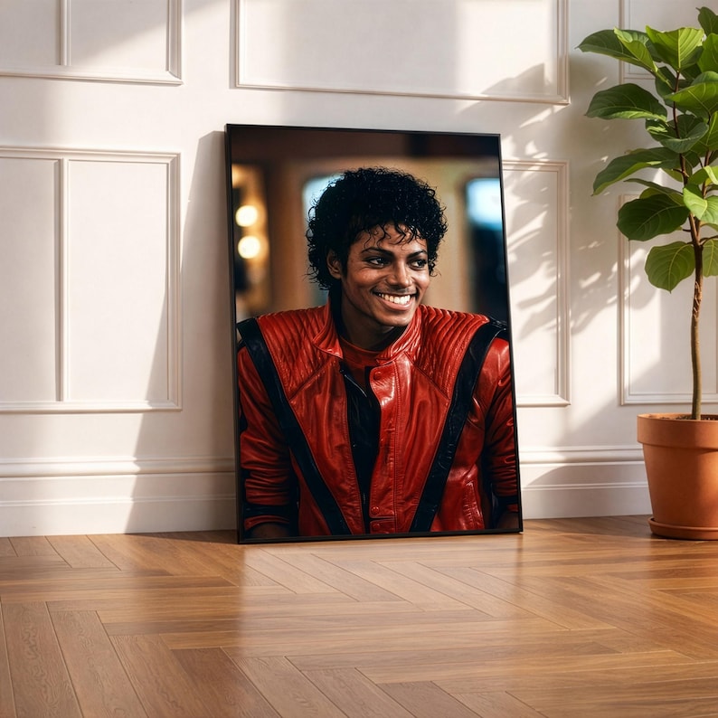 May include: A framed portrait of Michael Jackson, leaning against a white wall. The image features Jackson smiling, wearing a red leather jacket with black accents. The portrait is displayed on a wooden floor, with a potted plant in the background.