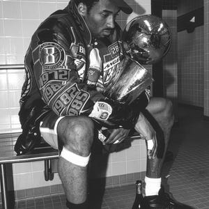 May include: Black and white image of a person wearing a baseball cap and a jacket with patches and the word "Champions" on the cap. The person is holding a trophy and a globe. There are two bottles and a towel on the floor.