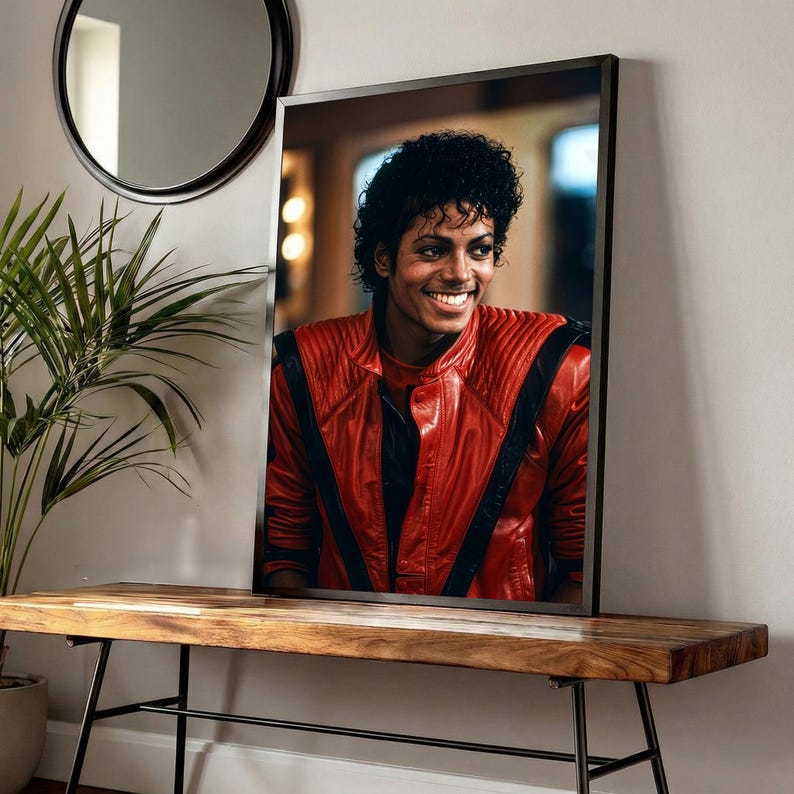 May include: Framed portrait of a smiling person wearing a red leather jacket with black accents. The portrait is displayed on a wooden bench with black metal legs, with a round mirror and a potted plant in the background.