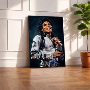 May include: A framed portrait of Michael Jackson, leaning against a white wall. The image shows Jackson smiling while holding a microphone. He is wearing a silver jacket with black accents and a decorative belt. A potted plant is in the background.