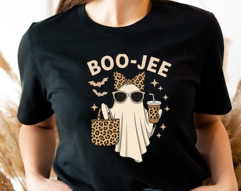 May include: A black t-shirt featuring a graphic of a ghost wearing sunglasses and a leopard print bow. The ghost holds a leopard print tote bag and a matching cup. The text BOO-JEE is printed above the ghost, accompanied by small bat and star icons.