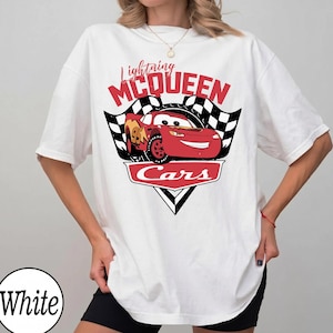 May include: White t-shirt featuring a graphic of Lightning McQueen from the Cars movie. The design includes the text "Lightning McQueen" above a red race car, with checkered flags and the word "Cars" below.