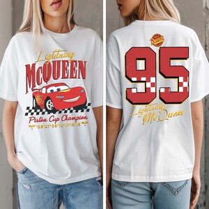 May include: White t-shirt featuring Lightning McQueen from the movie Cars. The front graphic includes the character, text "Lightning McQueen", and "Piston Cup Champion". The back displays a large "95" and "Lightning McQueen" in red and yellow.