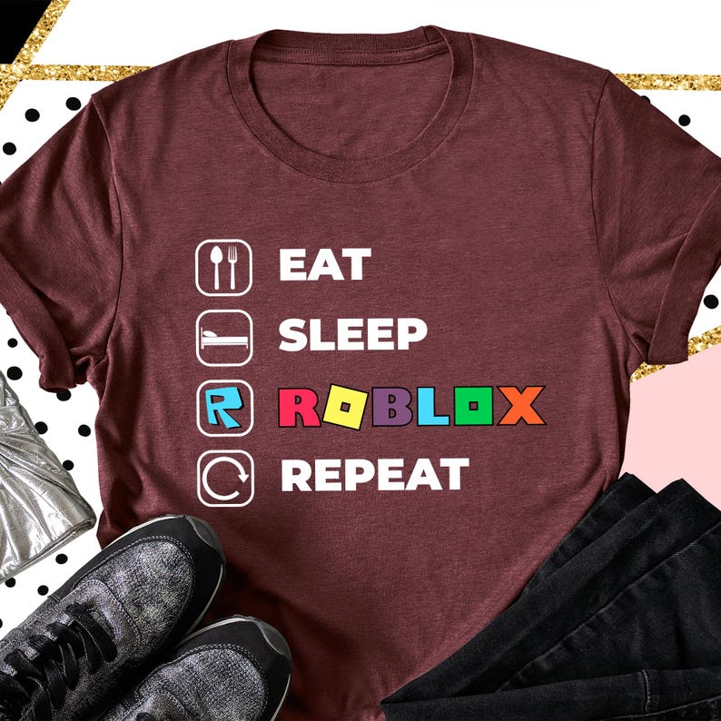 Puede incluir: Una camiseta de manga corta color granate con un estampado gr&aacute;fico blanco que muestra el texto EAT, SLEEP, ROBLOX y REPEAT. Cada palabra va acompa&ntilde;ada de un icono correspondiente, incluyendo cuchara y tenedor, una cama, el logo de Roblox y una flecha.