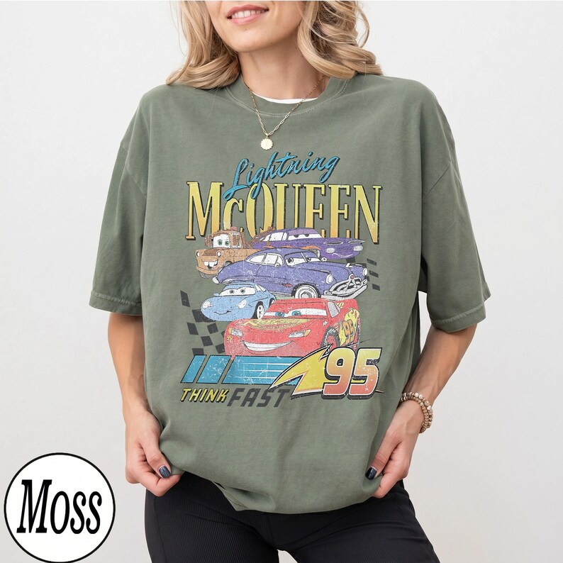 Puede incluir: Camiseta verde oliva con un dise&ntilde;o de Lightning McQueen y otros personajes de la pel&iacute;cula Cars. El dise&ntilde;o incluye el texto "Lightning McQueen", "95" y "Think Fast".