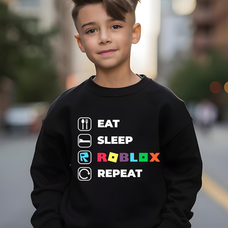 Puede incluir: Una sudadera negra de manga larga con un estampado gr&aacute;fico blanco con el texto EAT SLEEP ROBLOX REPEAT. El dise&ntilde;o incluye iconos de cuchara y tenedor, una cama, el logotipo de Roblox y una flecha circular, con la palabra ROBLOX en letras de colores.