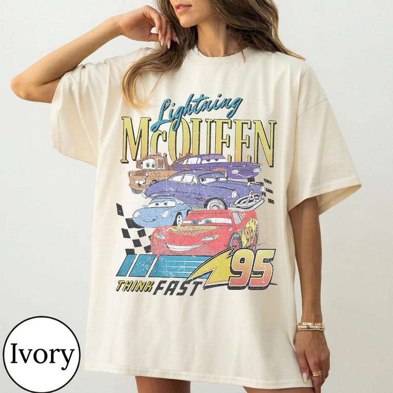 Puede incluir: Camiseta de color marfil con un gr&aacute;fico de Lightning McQueen y otros personajes de Cars. El dise&ntilde;o incluye el texto "Lightning McQueen", "95" y "Think Fast". La camiseta tiene mangas cortas y un corte holgado.