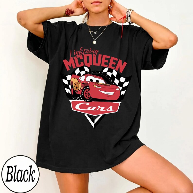 May include: Black t-shirt featuring a graphic of Lightning McQueen from the movie Cars. The design includes the text "Lightning McQueen" in red and the word "Cars" in white. A checkered flag design is also present.