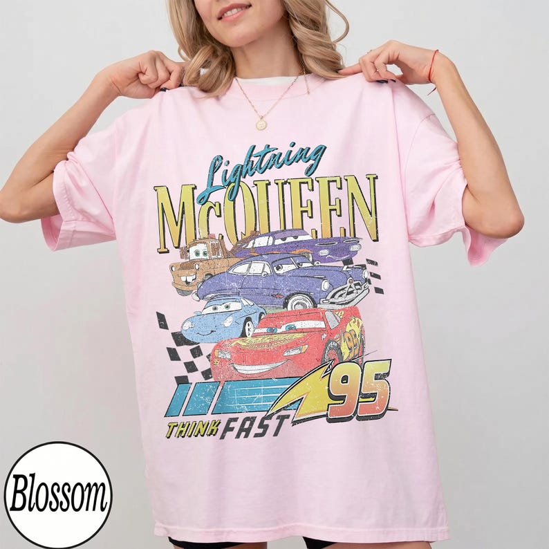 Puede incluir: Camiseta rosa claro con un dise&ntilde;o de Rayo McQueen y otros personajes de Cars. El dise&ntilde;o incluye el texto "Lightning McQueen", "95" y "Think Fast". La camiseta tiene mangas cortas y un corte holgado.