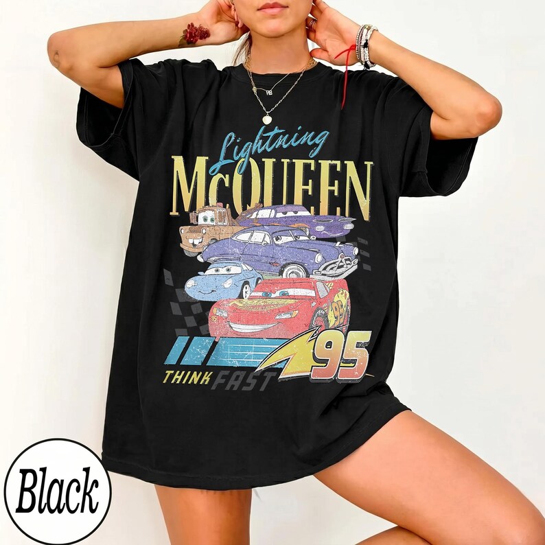 Puede incluir: Camiseta negra con un dise&ntilde;o de Rayo McQueen y otros personajes de Cars. El dise&ntilde;o incluye el texto "Lightning McQueen" en azul y dorado, con "Think Fast" y "95" debajo. La camiseta tiene un aspecto vintage y desgastado.