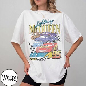 Puede incluir: Camiseta blanca con un dise&ntilde;o de Rayo McQueen y otros personajes de Cars. El dise&ntilde;o incluye el texto "Lightning McQueen" y "Think Fast 95" en un estilo vintage. La camiseta tiene un corte holgado y oversize.