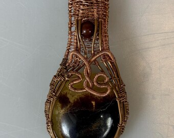 May include: A copper wire wrapped pendant featuring a brown and yellow agate stone. The pendant has a copper bead at the top.