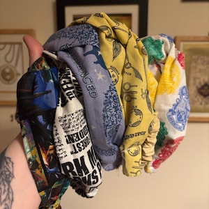 May include: A selection of patterned fabric headbands in various colours. The headbands display designs with text and images, including the words "FOREST", "SLUDGE", and "QUIDDITCH". The headbands are in shades of blue, yellow, and white.