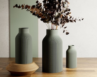 May include: Three green ceramic vases with a ribbed texture. The tallest vase is filled with dried brown and gray flowers. The vases are on a wooden surface.
