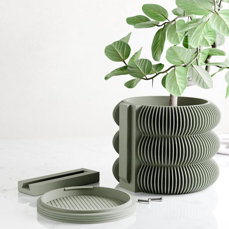 May include: A sage green, modern plant pot with a unique, ribbed design. The pot is holding a leafy green plant. A matching saucer and a rectangular piece are next to the pot. The pot is approximately 10 inches tall.