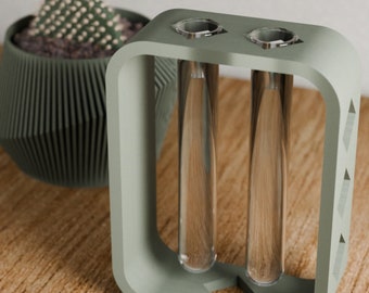 May include: A light green rectangular vase with two clear glass test tubes for holding flowers or greenery. The vase has a modern design with a geometric pattern.