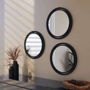 May include: Three black framed round mirrors of different sizes hanging on a wall. The mirrors are all circular and have a simple black frame.